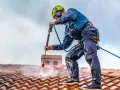Pracownik w kasku i zabezpieczeniach myje dach myjką ciśnieniową. Sprawdź, jaka jest mycie dachu cena i odśwież wygląd swojego domu.