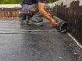 Budowlaniec rozwija papę izolacyjną na fundamencie.