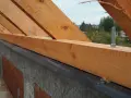 Drewniana murłata z widocznymi wymiarami, przykręcona do betonowej ściany. W tle drzewa i domy.