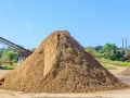 Duża hałda piasku na placu budowy, z taśmociągiem w tle.