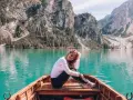 Uśmiechnięta kobieta siedzi w łodzi na turkusowym jeziorze, otoczona majestatycznymi górami **Dolomitów**.