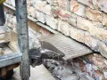 Prace przy izolacji fundamentów w starym domu. Widać fragment maszyny i ceglaną ścianę.