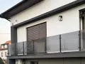 Nowoczesna balustrada z matowego szkła i czarnych słupków w kolorze RAL 9005, odbijająca drzewa.
