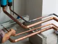 Instalator wykonuje lutowanie twarde miedzianych rur. Widać palnik i drut spawalniczy.