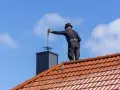Kominiarz w cylindrze wykonuje przegląd kominiarski, czyszcząc komin na dachu pokrytym dachówką.