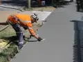Robotnik w pomarańczowej kamizelce wygładza świeży beton. Zastanawiasz się, ile kosztuje kubik betonu na taką pracę?