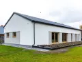 Nowoczesny dom z dachem dwuspadowym 100m2. Biała elewacja, duże okna, szary dach.