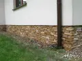 Eleganckie cokoliki z kamienia ozdabiają dom, tworząc naturalną, kamienną opaskę wokół białej ściany.
