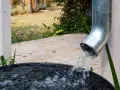 Woda z rynny spływa do czarnego zbiornika, zbierając deszczówkę.