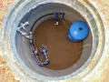 Wykończenie studni głębinowej: niebieski zbiornik hydroforowy i instalacja rurowa z manometrem.