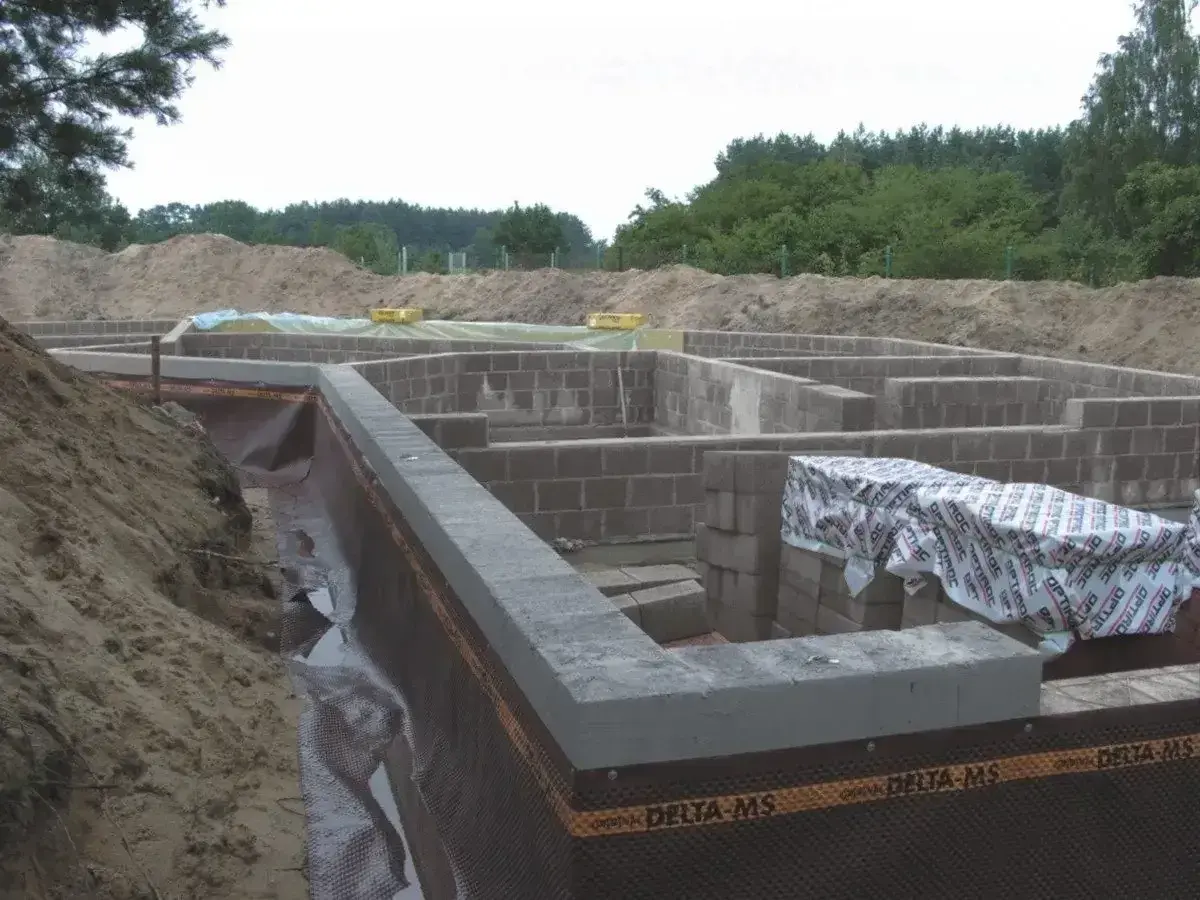 Fundament domu z bloczków betonowych, z widoczną izolacją i przygotowaniem pod keramzytobeton. Budowa w toku.