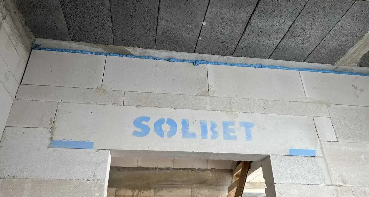 Piana montażowa tworzy dylatację między betonowymi stropami a ścianą z bloczków gazobetonowych. Na nadprożu widoczny napis "SOLBET".