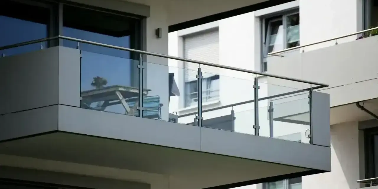 Nowoczesna loggia z przeszklonymi balustradami, na której stoi stolik z krzesłami.