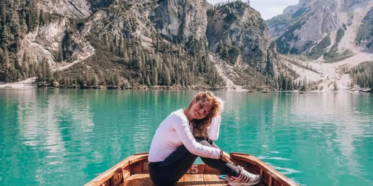 Uśmiechnięta kobieta siedzi w łodzi na turkusowym jeziorze, otoczona majestatycznymi górami **Dolomitów**.