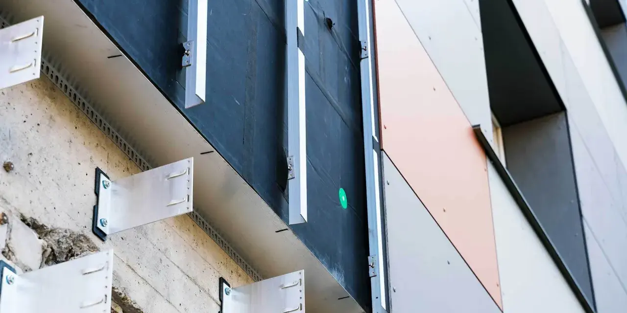 System mocowania paneli elewacyjnych. Widoczna betonowa ściana, izolacja i aluminiowe wsporniki tworzące przestrzeń dla wentylowanej elewacji.