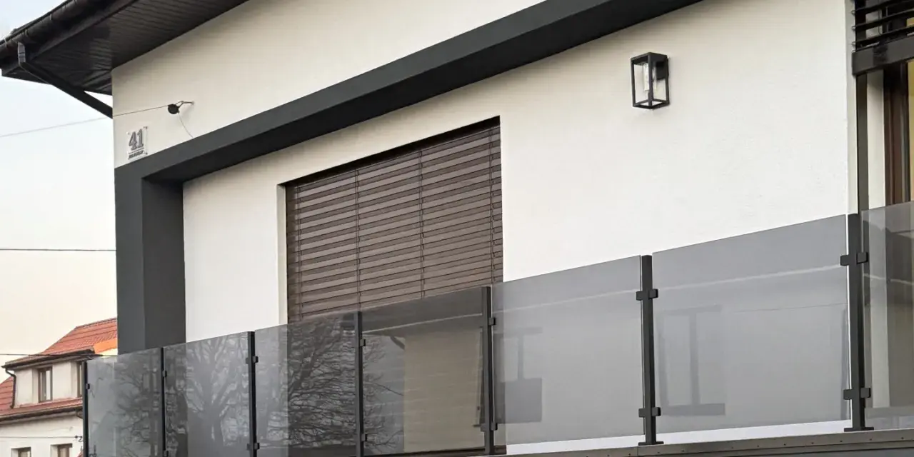 Nowoczesna balustrada z matowego szkła i czarnych słupków w kolorze RAL 9005, odbijająca drzewa.