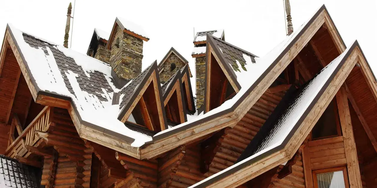 Drewniany dom z wieloma dachami i kominami, pokryty śniegiem. Widoczna jest jedna lukarna z kamiennym wykończeniem.