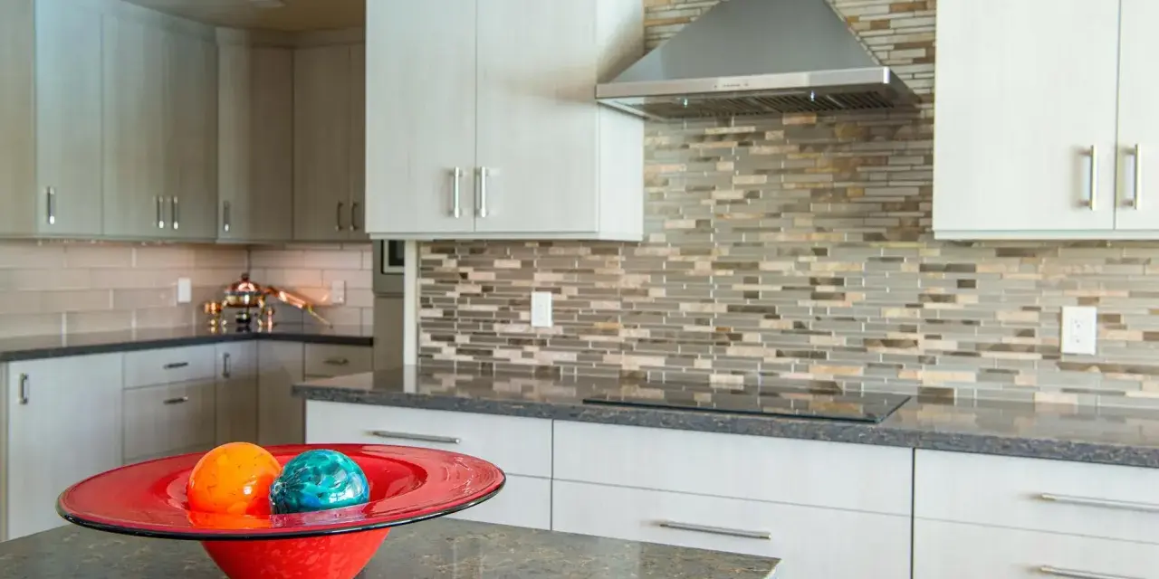 Nowoczesna kuchnia z jasnymi szafkami, mozaikową ścianą i blatem ze spieku kwarcowego. Na pierwszym planie czerwona misa z ozdobnymi kulami.