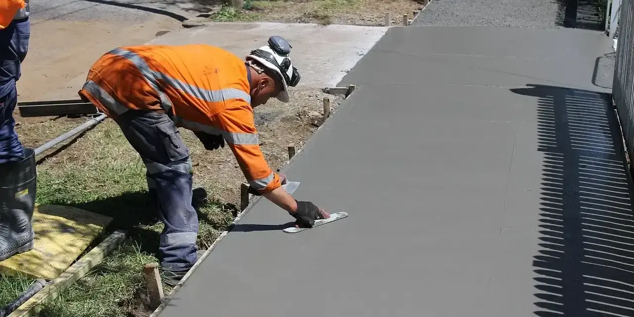 Robotnik w pomarańczowej kamizelce wygładza świeży beton. Zastanawiasz się, ile kosztuje kubik betonu na taką pracę?