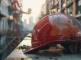 Czerwony kask budowlany, pokryty kurzem i brudem, leży na metalowej belce. W tle widać zarys budowy i dźwig. To znak, że wiecha na budowie jest blisko!