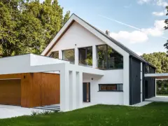 Nowoczesny biało-czarny dom z drewnianą bramą garażową, otoczony zielenią.