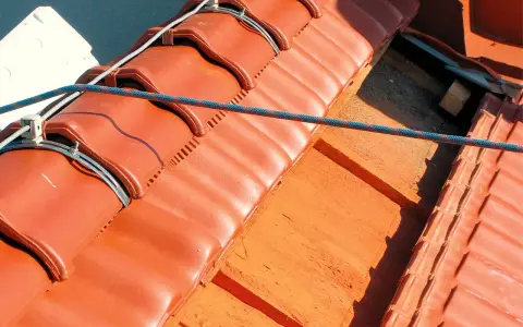 System piorunochronu na dachu z czerwonej dachówki, zabezpieczający przed uderzeniami pioruna.