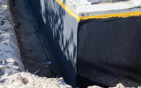 Czarne, izolowane betonowe ściany fundamentów, zabezpieczone przed wilgocią.