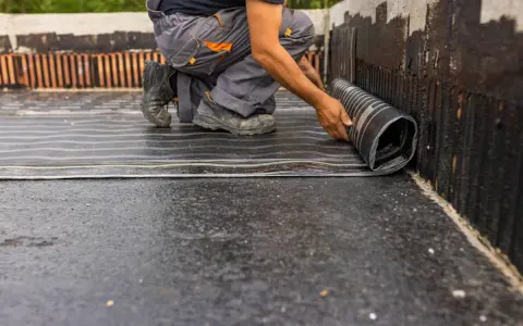 Budowlaniec rozwija papę izolacyjną na fundamencie.