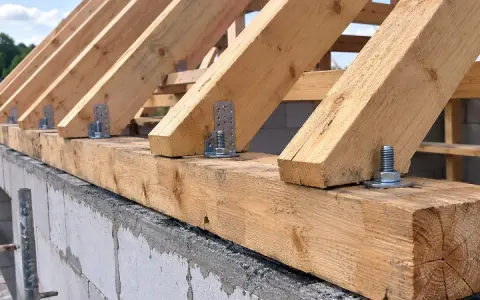 Drewniana konstrukcja dachu, gdzie krokwie są mocowane do murłaty za pomocą metalowych kątowników i śrub.