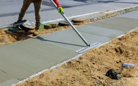 Robotnik wygładza świeży beton B25 na chodniku. Właściwe proporcje składników zapewniają trwałość nawierzchni.