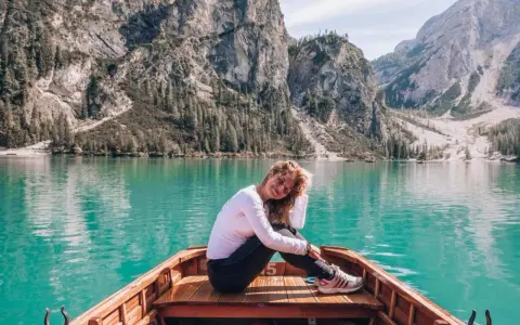 Uśmiechnięta kobieta siedzi w łodzi na turkusowym jeziorze, otoczona majestatycznymi górami **Dolomitów**.