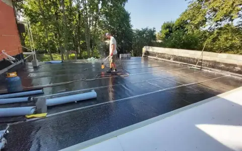 Pracownik wykonuje hydroizolację tarasu nad garażem, używając palnika do zgrzewania papy.