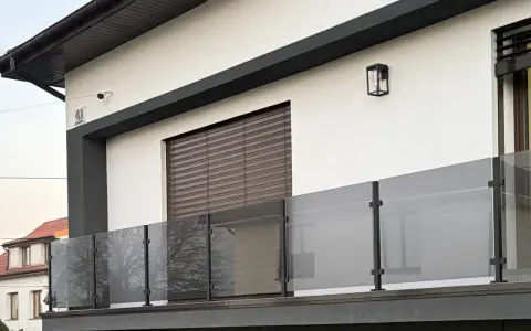Nowoczesna balustrada z matowego szkła i czarnych słupków w kolorze RAL 9005, odbijająca drzewa.