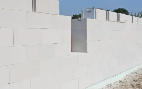 Ściana z bloczków suporeks wznoszona na budowie. Widać poziome linie ułatwiające murowanie i fragment fundamentu.