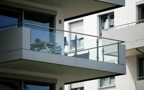 Nowoczesna loggia z przeszkloną balustradą, na której stoi stolik z kwiatami i krzesło.