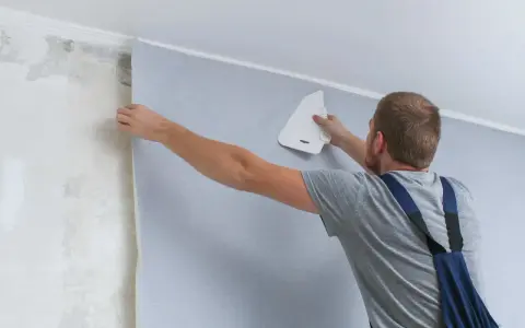 Mężczyzna przykleja tapetę. Zastanawiasz się nad tapetowanie cena?