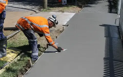 Robotnik w pomarańczowej kamizelce wygładza świeży beton. Zastanawiasz się, ile kosztuje kubik betonu na taką pracę?
