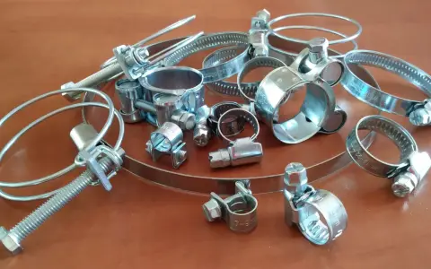 Metalowe opaski zaciskowe, czyli trytytki, w różnych rozmiarach, leżą na drewnianym blacie.