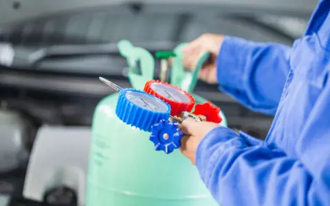 Mechanik podłącza manometry do butli z czynnikiem R32, przygotowując się do serwisu klimatyzacji samochodowej.