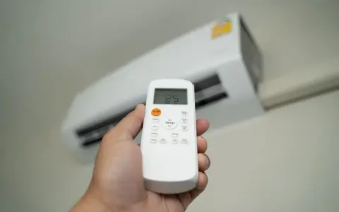 Dłoń trzymająca pilot do klimatyzatora, ustawiająca temperaturę 25°C. Ogrzewanie klimatyzatorem to komfort.
