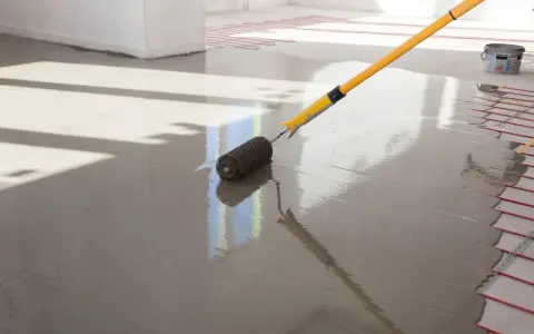 Wylewki anhydrytowe cena za 1m2. Wałek dociskowy rozprowadza świeżą masę po podłodze z ogrzewaniem podłogowym.