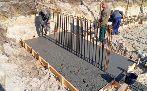 Budowa fundamentów: pracownicy wylewają beton, przygotowując zbrojenie pod przyszły żelbeton.
