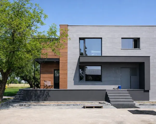 Nowoczesny dom z betonowych bloczków i drewna, nawiązujący stylem do **elewacji domów z lat 70-tych**, ale z odświeżonym, minimalistycznym charakterem.