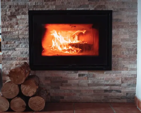 Płonące polana w nowoczesnym kominku, obłożonym kamieniem. Idealne miejsce, by zastanowić się, czy można palić w kominku.