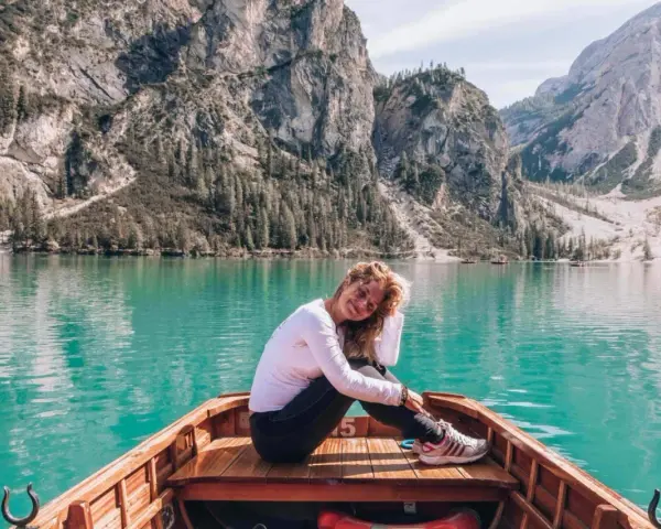 Uśmiechnięta kobieta siedzi w łodzi na turkusowym jeziorze, otoczona majestatycznymi górami **Dolomitów**.
