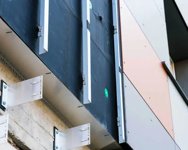 System mocowania paneli elewacyjnych. Widoczna betonowa ściana, izolacja i aluminiowe wsporniki tworzące przestrzeń dla wentylowanej elewacji.