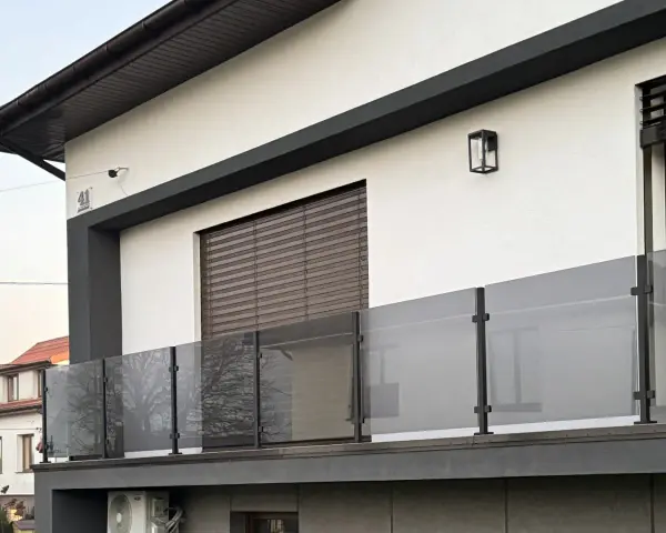 Nowoczesna balustrada z matowego szkła i czarnych słupków w kolorze RAL 9005, odbijająca drzewa.