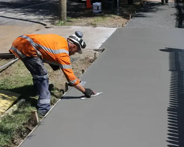 Robotnik w pomarańczowej kamizelce wygładza świeży beton. Zastanawiasz się, ile kosztuje kubik betonu na taką pracę?