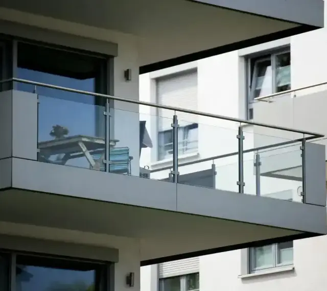Nowoczesna loggia z przeszklonymi balustradami, na której stoi stolik z krzesłami.