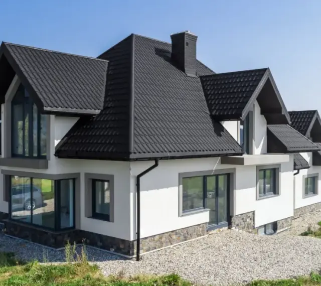Nowoczesny dom z białym tynkiem i kamienną podmurówką, z charakterystycznym, wielospadowym dachem. Konstrukcja dachu czterospadowego jest solidna i estetyczna.